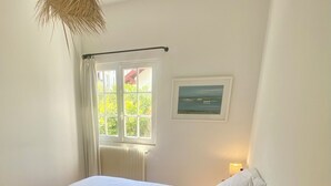 A bedroom with a large bed, a window with curtains, a radiator, a framed picture on the wall, and a hanging light fixture. - Quartier des Abatilles, Maison des Années 50 Rénovée, Proximité Plages, Forêt (Arcachon)