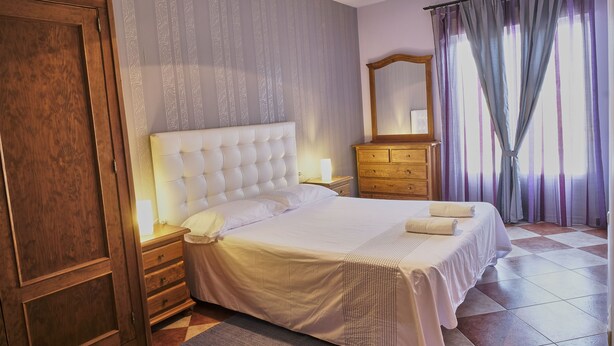 Un dormitorio con una cama grande, mesitas de noche de madera, un aparador y un espejo.