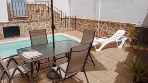 Una mesa de vidrio con sillas, una piscina, un muro de piedra y una parrilla.