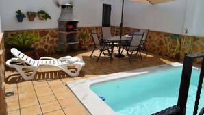 Un área de piscina con una parrilla, sillas de descanso y una mesa con sombrilla.