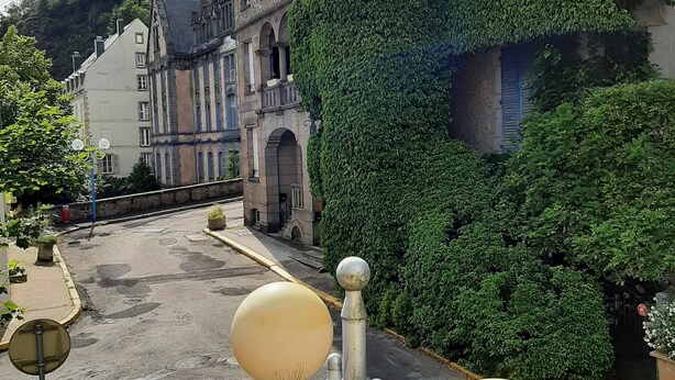 A street with a historic building, a roundabout, and a parked car. - Appartement F1 Tout Confort , en Centre Ville, Proche des Thermes (LA BOURBOULE)