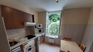 A compact kitchen with a sink, microwave, stove, and a small dining area with a table and chairs. - Appartement F1 Tout Confort , en Centre Ville, Proche des Thermes (LA BOURBOULE)
