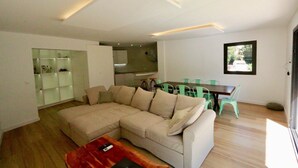 A modern living room with a sectional sofa, a dining table with chairs, and a kitchen in the background. - Apartamento-casa de Diseño con Entrada Privada y Pequeña Piscina (ses Illetes)