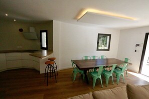 Eine moderne Küche mit Holzarbeitsplatte und Barhocker, ein Essbereich mit Holztisch und grünen Stühlen sowie ein großes Fenster für natürliches Licht.