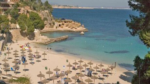 A beach with umbrellas and people, a rocky outcrop, and buildings in the background. - Apartamento-casa de Diseño con Entrada Privada y Pequeña Piscina (ses Illetes)