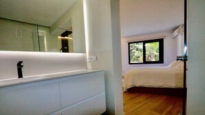 A modern bedroom with a large window, a white bed, and a built-in white vanity with a mirror. - Apartamento-casa de Diseño con Entrada Privada y Pequeña Piscina (ses Illetes)
