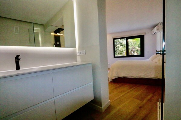 Une chambre à coucher moderne avec une grande fenêtre, un lit blanc et une coiffeuse blanche intégrée, dotée d’un miroir.