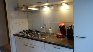 A modern kitchen with white cabinets, a stainless steel sink, a gas stove, a red kettle, and a coffee maker.