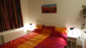 A bedroom with a bed, a radiator, a painting, a plant, and bedside lamps.