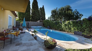 Una zona de piscina con patio de piedra, muebles de exterior y plantas en macetas.