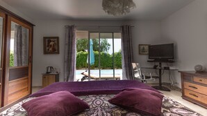 Un dormitorio con cama, televisión, escritorio y vistas a una piscina y vegetación.