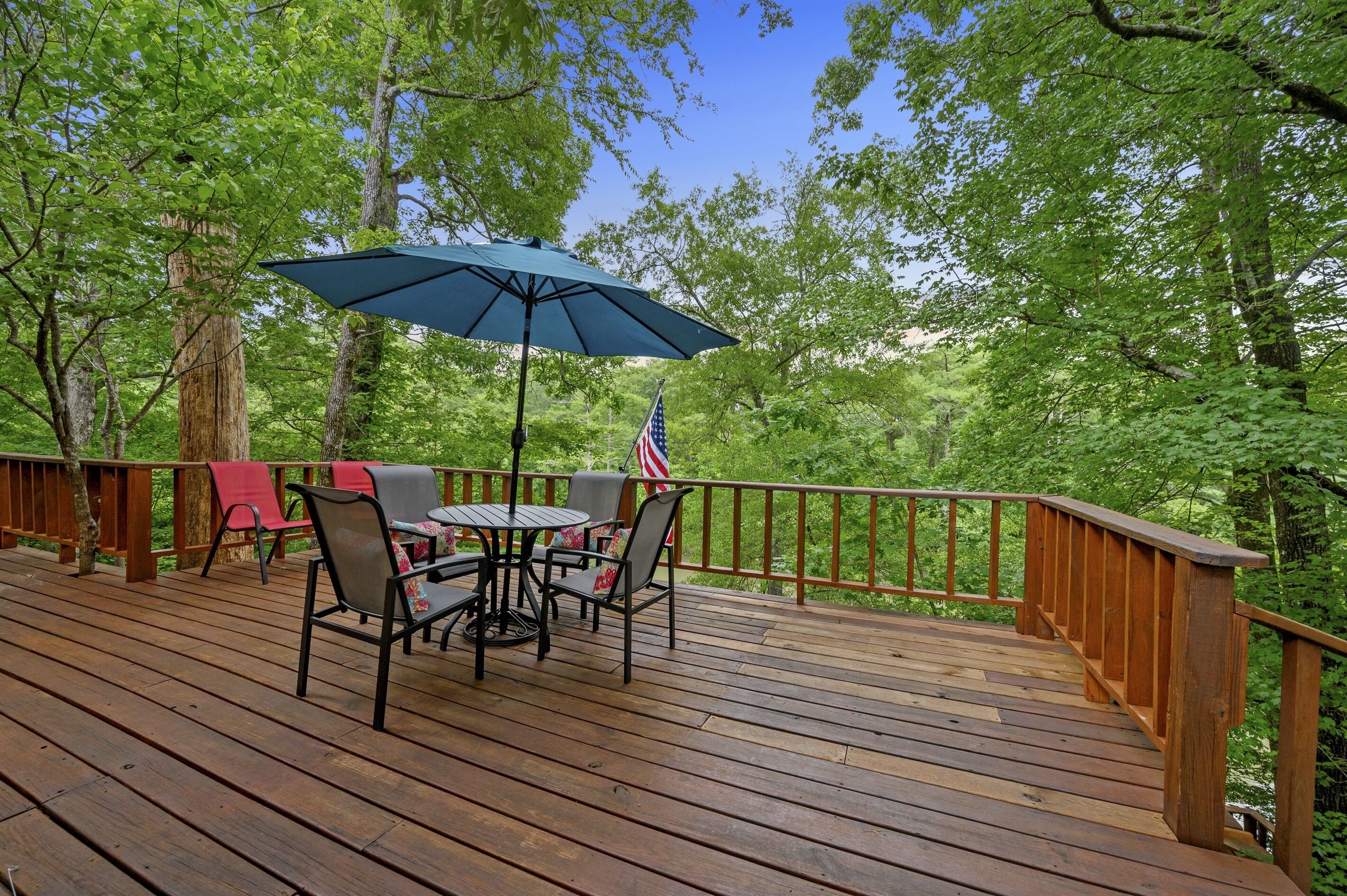 A wooden deck with a table and chairs, an American flag, and a blue umbrella.