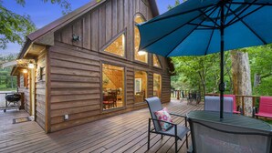 Una cabaña de madera con ventanas grandes, una terraza y asientos exteriores.