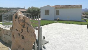 A white building with a tiled roof, a stone wall, and a metal gate. - Villa a 600m dal Mare (Budoni)