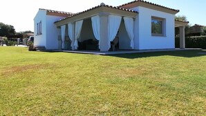 A white building with a tiled roof and a covered porch with white curtains. - Villa a 600m dal Mare (Budoni)