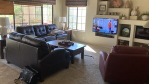 A living room with a leather sofa, a red armchair, a coffee table, and a television on a stand. - 2 bed 2 bath condo (Fountain Hills)