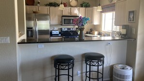 A kitchen with a central island, stainless steel appliances, and two bar stools. - 2 bed 2 bath condo (Fountain Hills)