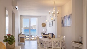 Un coin repas avec une table dressée pour quatre personnes, un lustre et une vue sur la mer grâce à de grandes fenêtres.