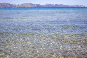 A clear view of a beach with shallow water and distant mountains.