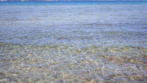 On aperçoit clairement une plage, avec une eau peu profonde et des montagnes au loin.