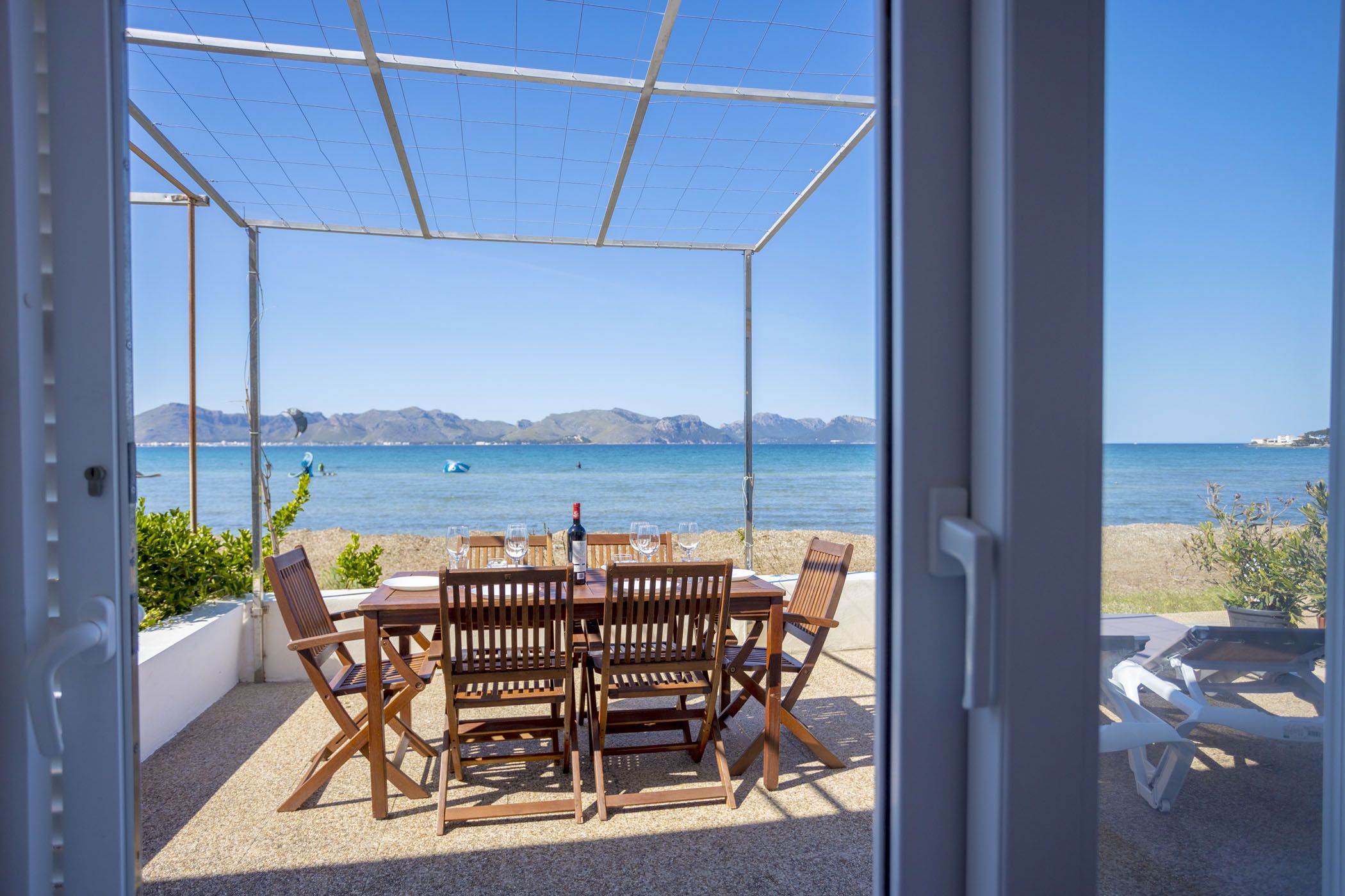 Un espace extérieur abrité, avec une table et des chaises, offrant une vue sur une plage et la mer.