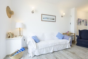 A white sofa with blue cushions, a lamp, a framed picture, and a wall-mounted light fixture in a living room.