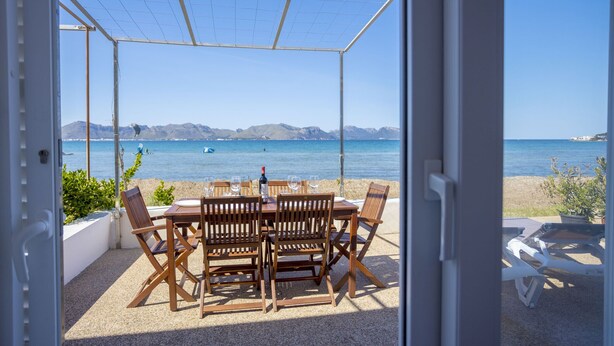 Un espace extérieur abrité, avec une table et des chaises, offrant une vue sur une plage et la mer.
