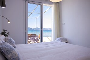 A bedroom with a bed, a chair, and a view of the sea through a glass door. - House on the seafront with 3 bedrooms, 2 bathrooms and barbecue (Alcúdia)