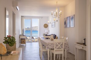 Ein Essbereich mit einem Tisch für vier Personen, einer Chandelüster und Blick auf das Meer durch große Fenster.