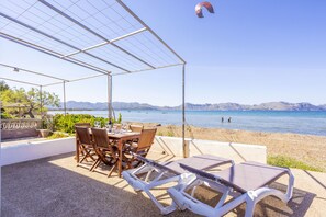 Ein überdachter Außenbereich mit Tisch und Stühlen mit Blick auf einen Strand und das Meer.