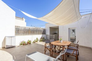 Eine Terrasse mit einem runden Holztisch und Stühlen, einem weißen Schrank und Topfpflanzen.