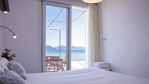 Une chambre à coucher avec un lit, une chaise et une vue sur la mer, visible à travers une porte vitrée.