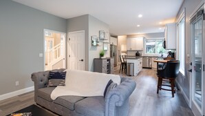 A modern living room with a grey sofa, a coffee table, and a kitchen in the background. - Entire 4-bedroom house, billiards and ping-pong, close to University of Oregon (Eugene)