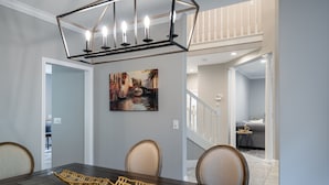 A dining area with a dark wooden table, beige chairs, and a geometric chandelier. A painting of a canal scene is on the wall. - Entire 4-bedroom house, billiards and ping-pong, close to University of Oregon (Eugene)