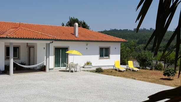 A house with a tiled roof, a covered patio with chairs and an umbrella, and a view of the surrounding landscape.