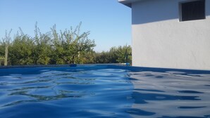 A swimming pool with clear blue water, surrounded by trees and a white building with a window.