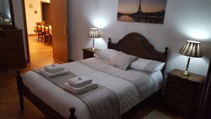A neatly made bed with white linens and two pillows, a wooden headboard, and two bedside lamps.