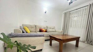 A living room with a sofa, a wooden coffee table, and a potted plant. - Neema Executive Suites Near Junction Mall 5A (Nairobi)