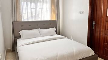 A neatly made bed with a grey headboard, white bedding, and a wooden door to the right.