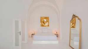 A bedroom with a white bed, a large mirror, and a decorative wall piece. - Sophia Privilege (Santorini)