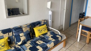 Una habitación con sofá, televisión instalada en la pared, aire acondicionado blanco y una mesa de comedor con sillas.