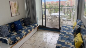 Un balcón con una mesa y sillas de comedor, un sofá y un ventanal corredero que da a vistas de edificios.