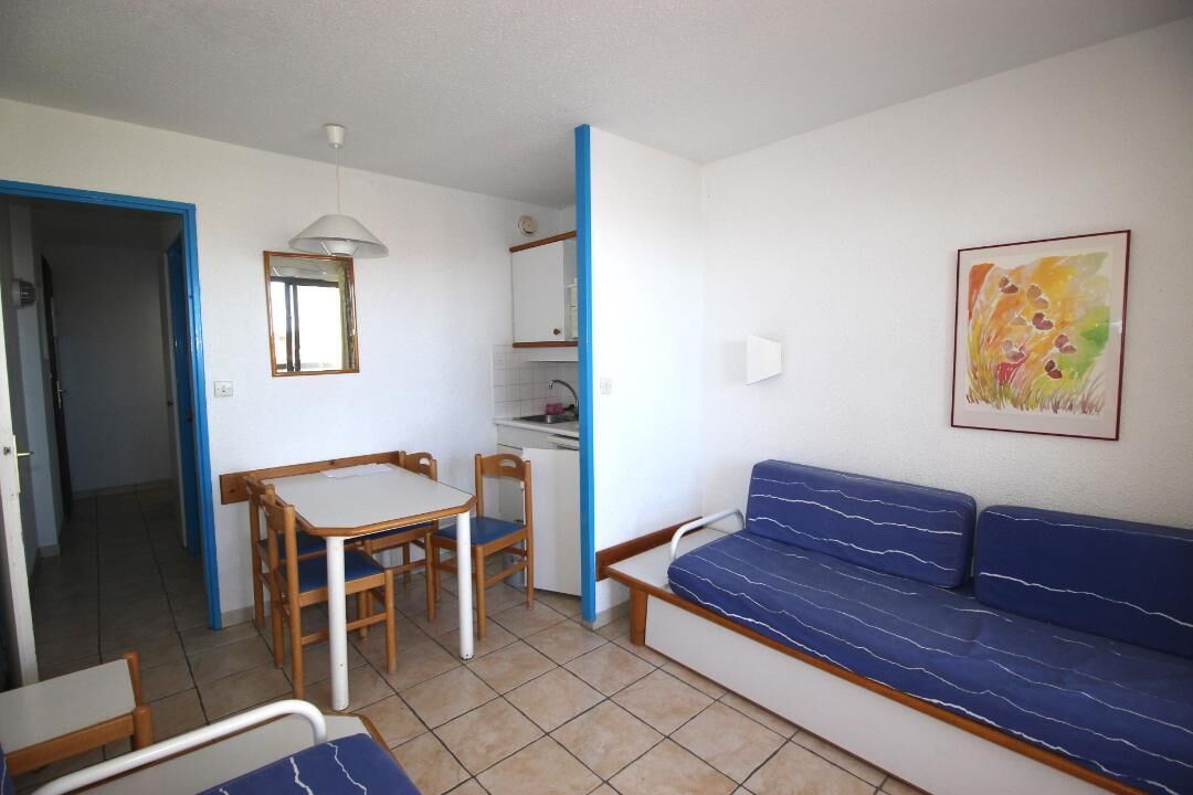 Ein gemütlicher Raum mit einem blau gestreiften Sofa, einem kleinen Esstisch mit Stühlen, einem Spiegel und einem gerahmten Gemälde an der Wand.