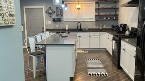 A modern kitchen with a central island, white cabinetry, a black stove, and pendant lighting.