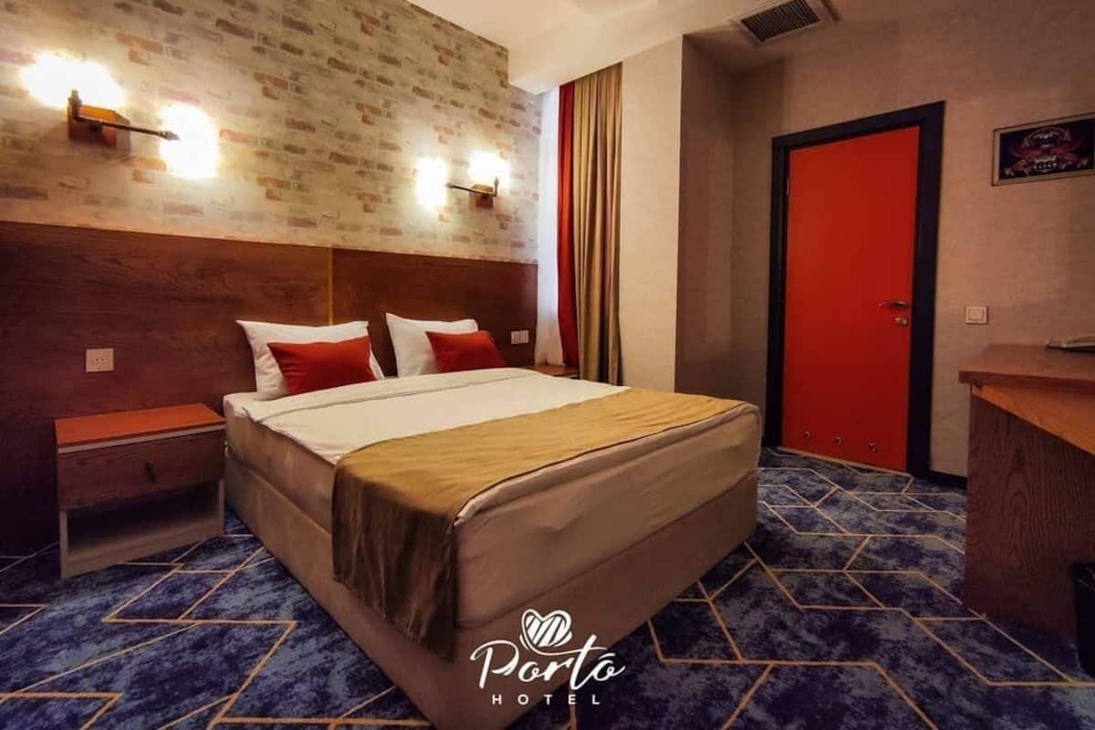 Ein Hotelzimmer mit Bett, Nachttischen, Schreibtisch und einer roten Tür.