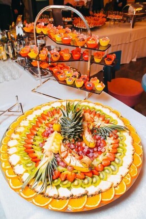 Et fad med frugt, forskellige skiveskåret frugter og en ananas i midten, omgivet af en lagdelt dessertudstilling.