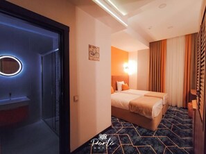 A hotel room with a bed, a nightstand, a mirror with a circular light, and a wall-mounted light fixture. - Porto Hotel Baku (Baku)