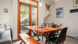A dining area with a wooden table, black chairs, and a bench. There is a poster on the wall and a window with blinds. - 2BR | Symphony | Dog Friendly | Hot Tub | Private Balconies | Village Location | Parking (Whistler)