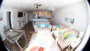 A modern kitchen with a dining area, a living room with a sofa and a coffee table, and a ceiling fan.
