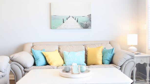A living room with a beige sofa, a white coffee table, and a painting of a pier.